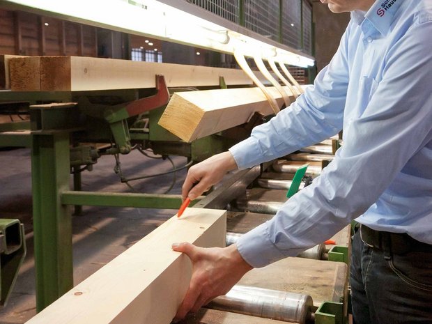 [Translate to Italienisch:] Messung und Anpassung von Holz durch Person in der Produktionshalle der SchwörerHaus KG